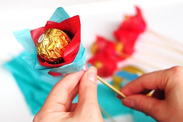 Eine Frau stellt eine Blüte aus Praline, Spieß und Papier her