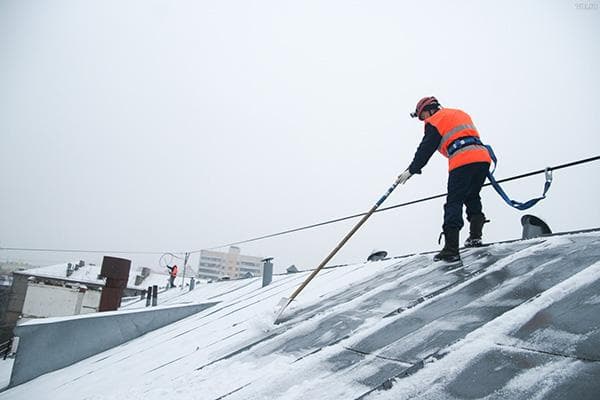 Ein Mitarbeiter der Hausverwaltung reinigt ein Falzdach von Schnee