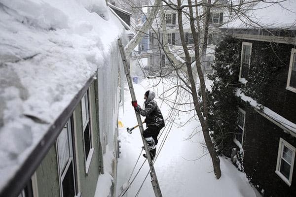 Ein Mann klettert auf ein verschneites Dach über eine Leiter