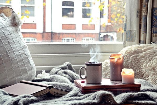 Decke, Kerzen, Buch und eine Tasse heißen Tee