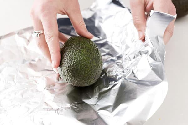 Eine Frau wickelt eine Avocado in Alufolie
