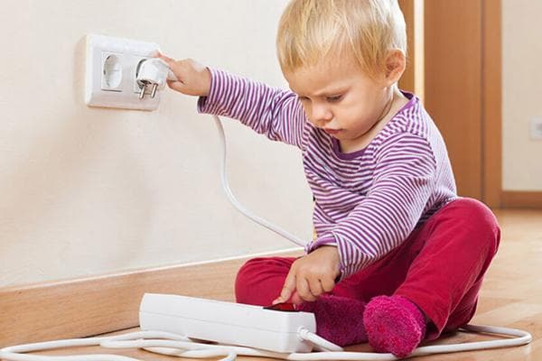 Kind steckt den Stecker einer Steckdosenleiste in die Steckdose