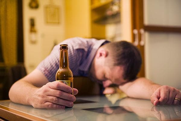 Ein betrunkener Mann mit einer Bierflasche am Tisch