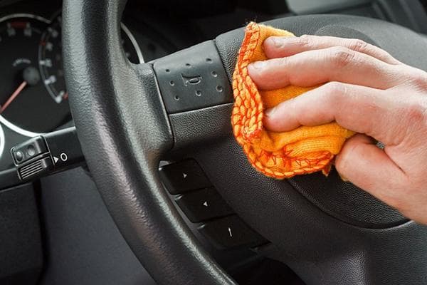 Ein Mann wischt das Lenkrad im Auto mit einem Tuch ab