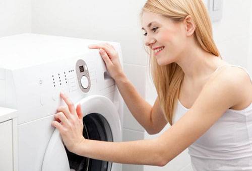 Eine junge Frau schaltet die Waschmaschine aus.