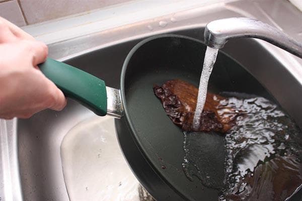 Eine Pfanne unter dem Wasserhahn waschen
