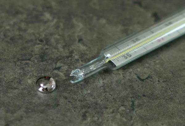Zerbrochenes Thermometer zusammen mit dem gesammelten Quecksilber