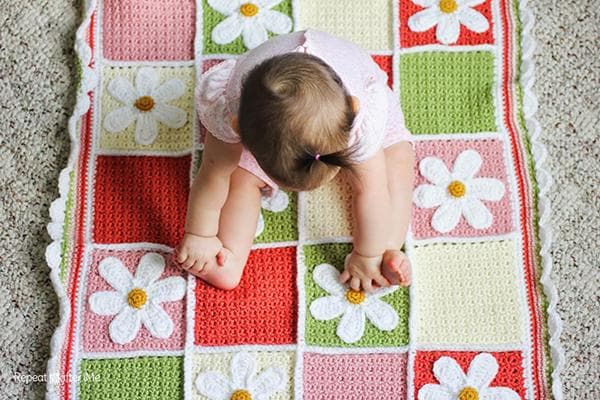 Ein kleines Mädchen sitzt auf einem gestrickten Teppich