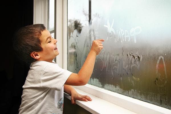 Ein Kind schreibt auf ein beschlagenes Fenster