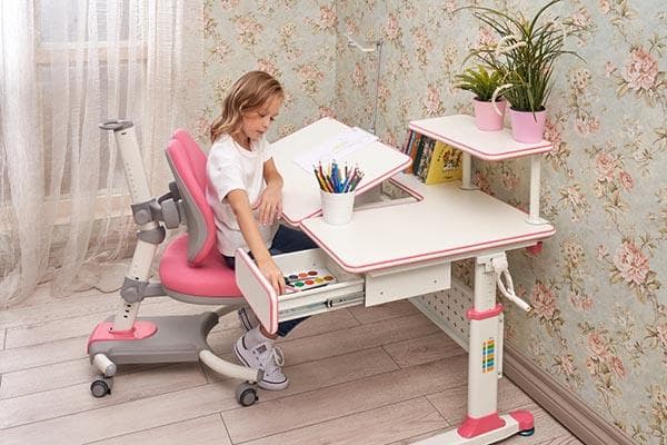 Ein Mädchen holt Büromaterial aus der Schublade eines Schreibtisches