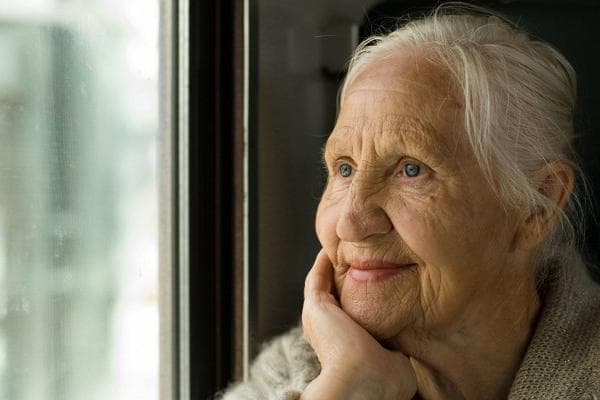 Eine ältere Frau erinnert sich an etwas am Fenster