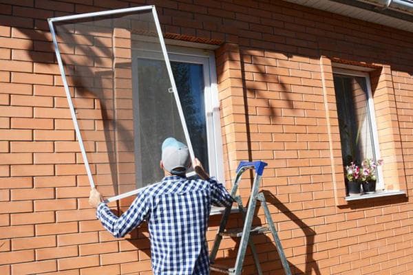 Ein Mann entfernt ein Moskitonetz von einem Fenster eines Einfamilienhauses