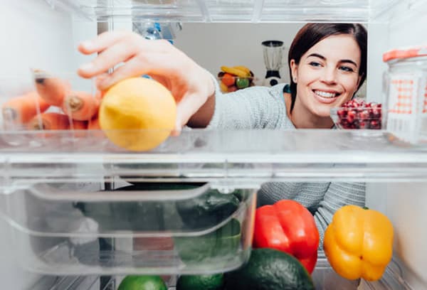 Eine Frau legt eine Zitrone in den Kühlschrank