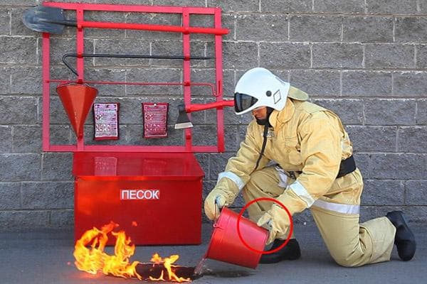 Ein Feuerwehrmann löscht Flammen mit Wasser aus einem Eimer