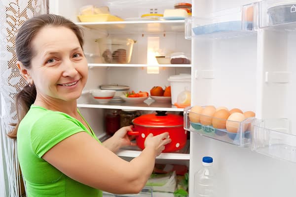 Eine Frau stellt einen Topf in den Kühlschrank