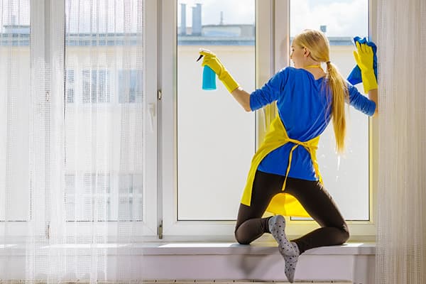 Eine Frau auf der Fensterbank putzt das Fenster