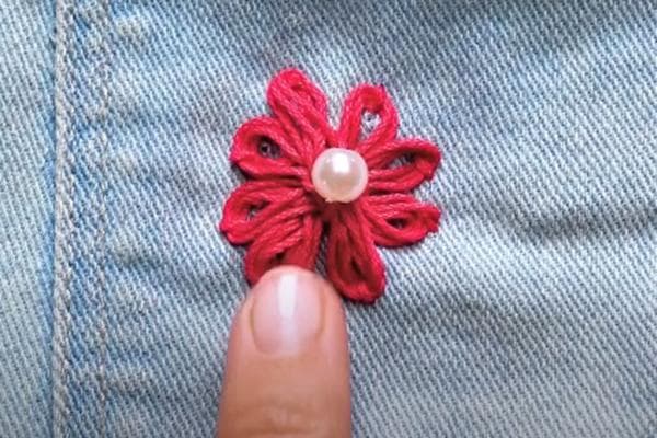 Eine Blume, die mit dicken Fäden auf die Jeans gestickt wurde