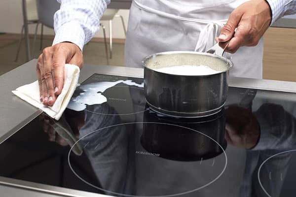 Ein Koch wischt verschüttete Milch von einem Induktionskochfeld