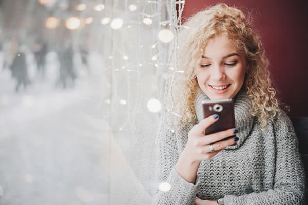 Frau mit Smartphone am Fenster mit Girlande