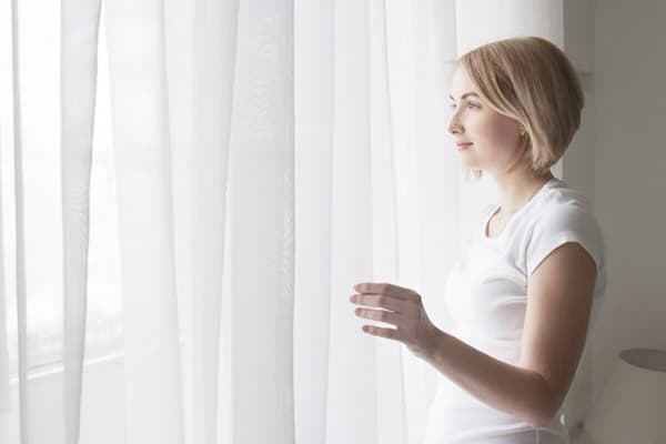 Mädchen am Fenster mit einer weißen Gardine