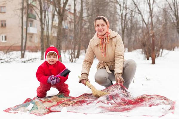 Frau mit Kind reinigt einen Teppich im Schnee